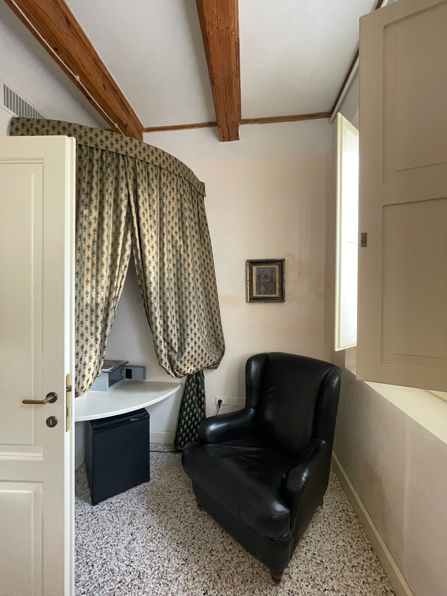 A corner room with a black leather chair, a white door, a small white table, and a patterned curtain.