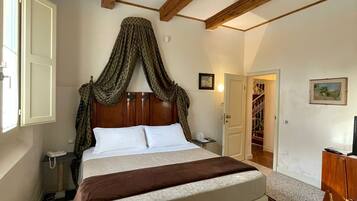 A bedroom with a wooden ceiling, a canopy bed, a bedside table, a chair, and a desk.