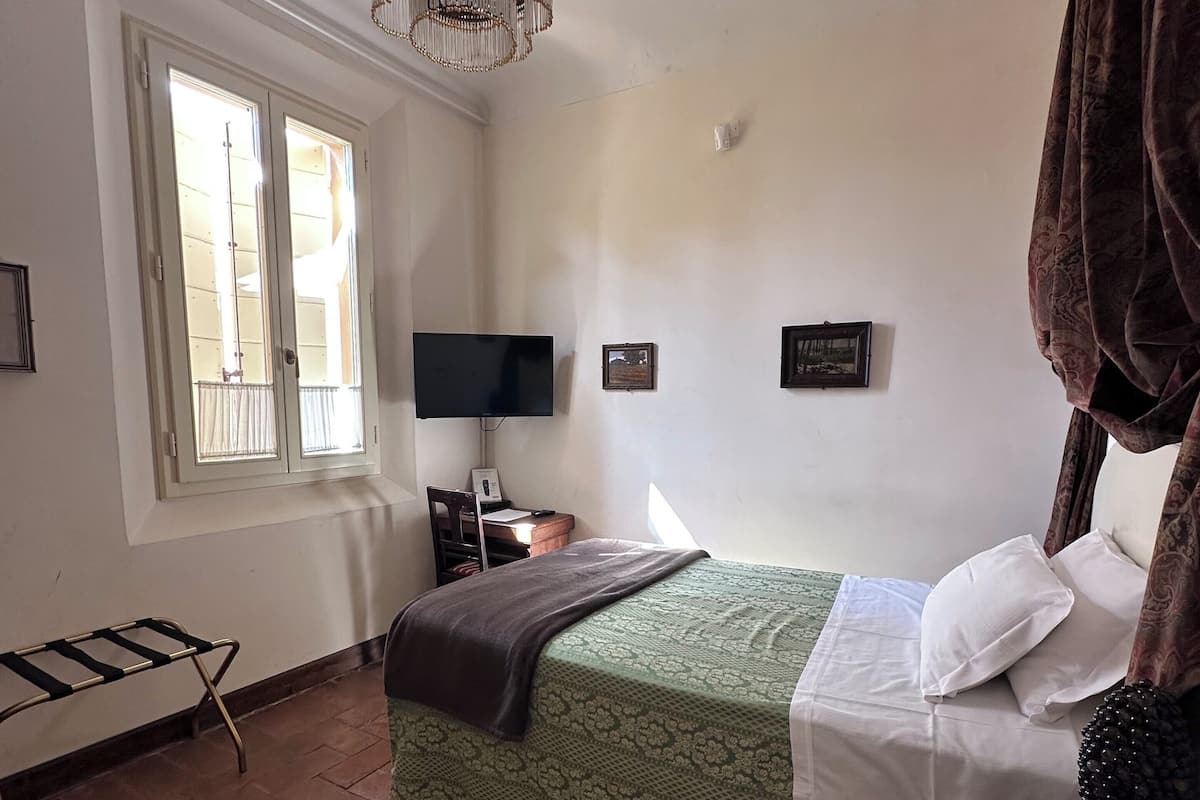 Un dormitorio con cama, televisión, candelabro, ventana y teléfono.