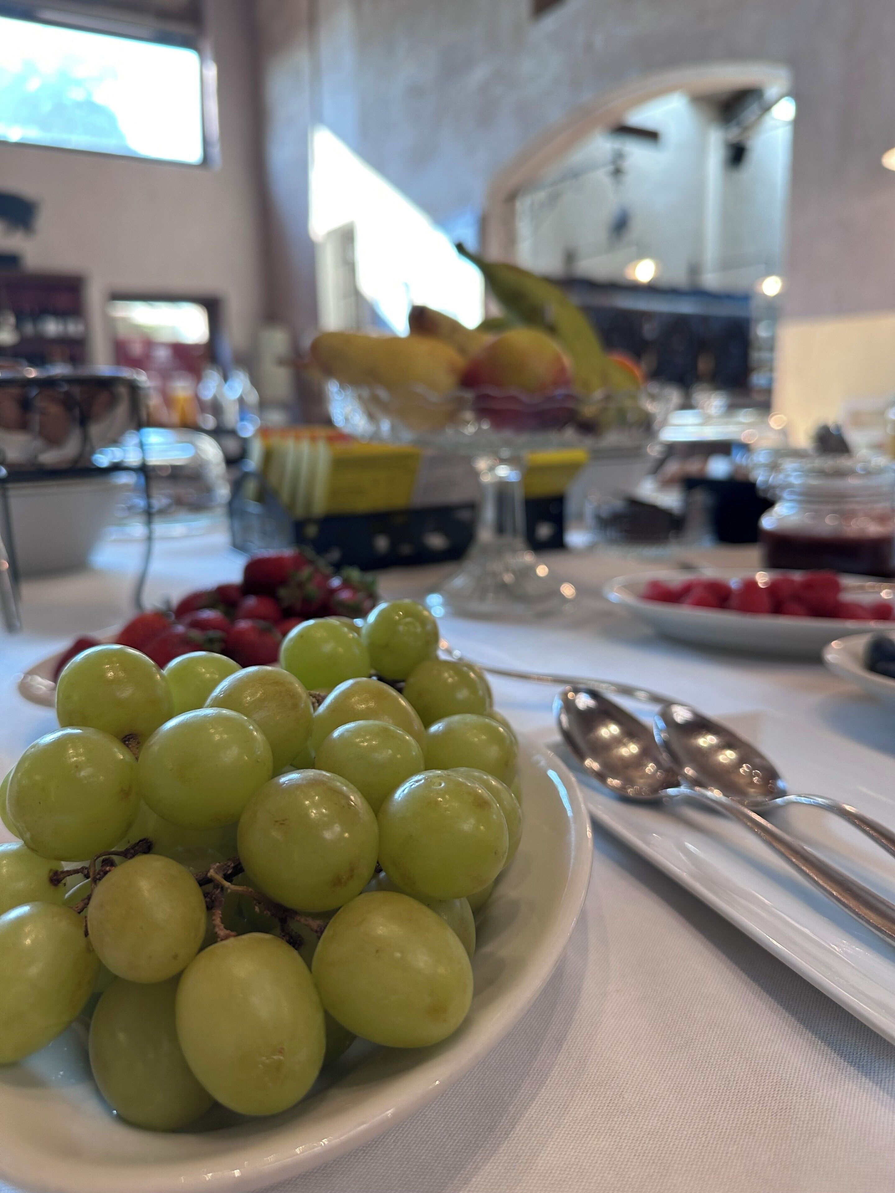 Una mesa con un bol de uvas verdes, una bandeja de fruta y una cuchara.