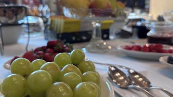 Una mesa con un bol de uvas verdes, una bandeja de fruta y una cuchara.