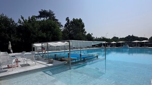 Ein Schwimmbad mit gefliestem Boden, weißen Liegestühlen und Sonnenschirmen.