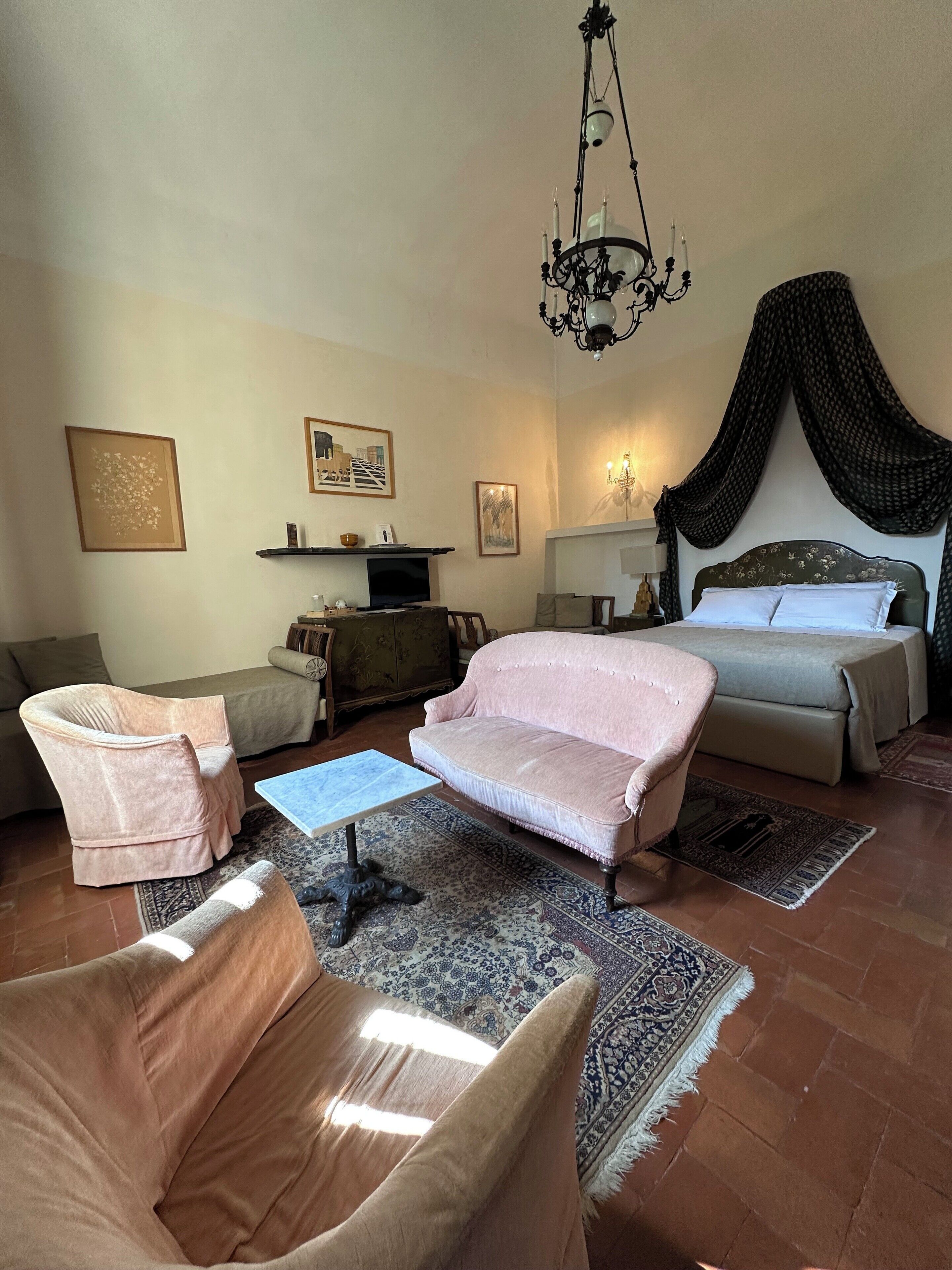 A living room with a sofa, armchair, and a television. There is a bed with a canopy and a chandelier.