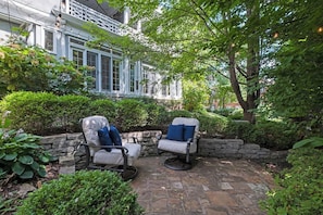 A patio with two chairs and a stone wall. - Southmoreland Mansion-Sleeps 28! (Kansas City)
