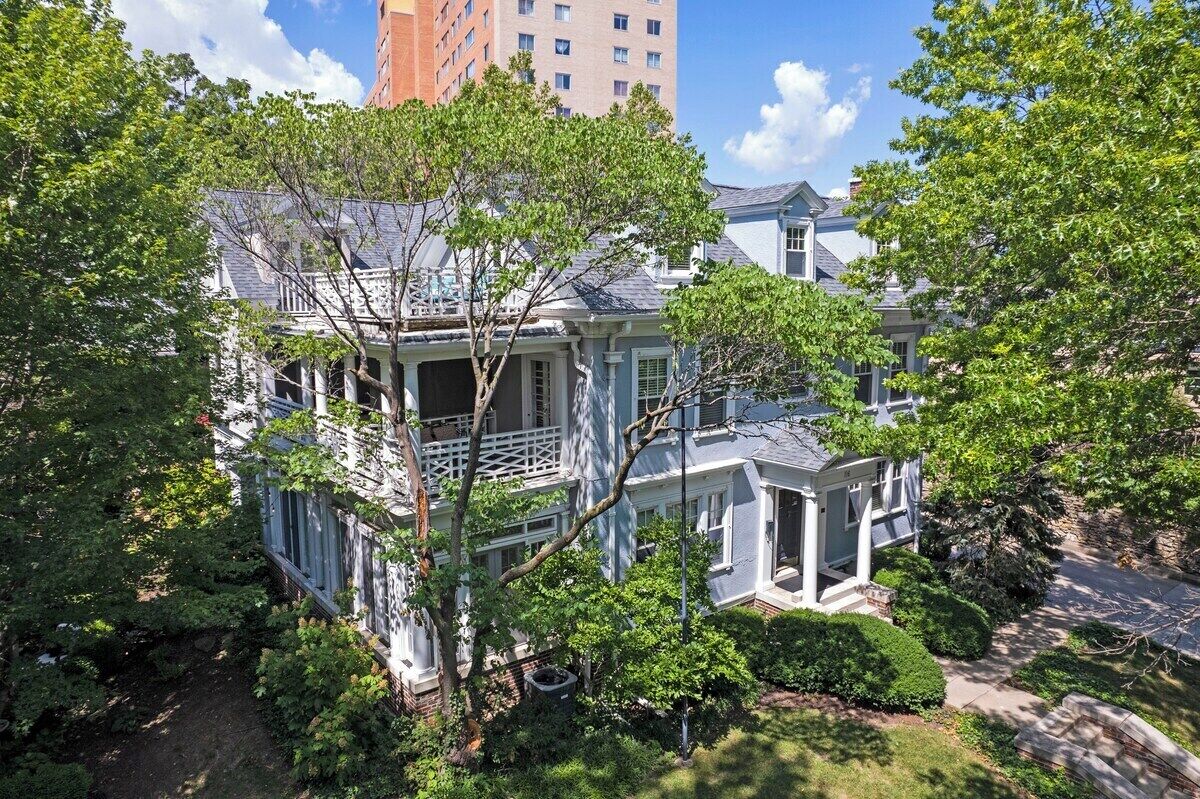 A two-story house with a balcony, surrounded by lush greenery and a clear sky.