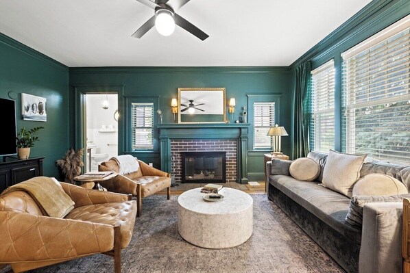 A living room with a fireplace, leather sofas, a round coffee table, and a ceiling fan.