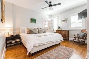 Un dormitorio con cama, mesita de noche, cómoda, silla y ventilador de techo.