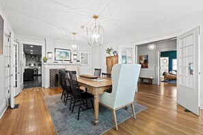 A spacious dining area with a wooden table and chairs, a chandelier, and a view into the kitchen.