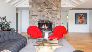 Ein modernes Wohnzimmer mit Kamin aus Stein, roten Sesseln, einem Glastisch und einem großen Sofa.