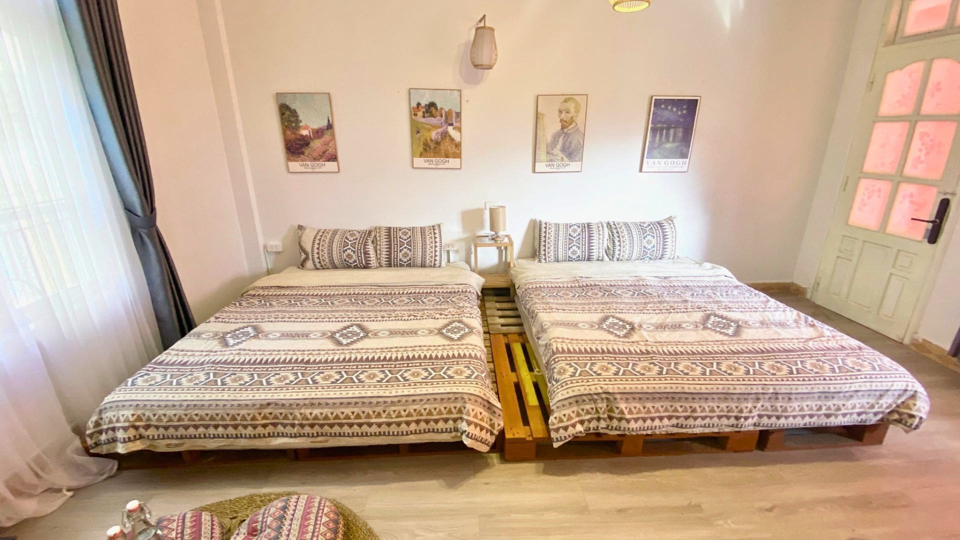 Une chambre double avec deux lits, une literie à motifs, une petite table et des œuvres d’art murales représentant Van Gogh.