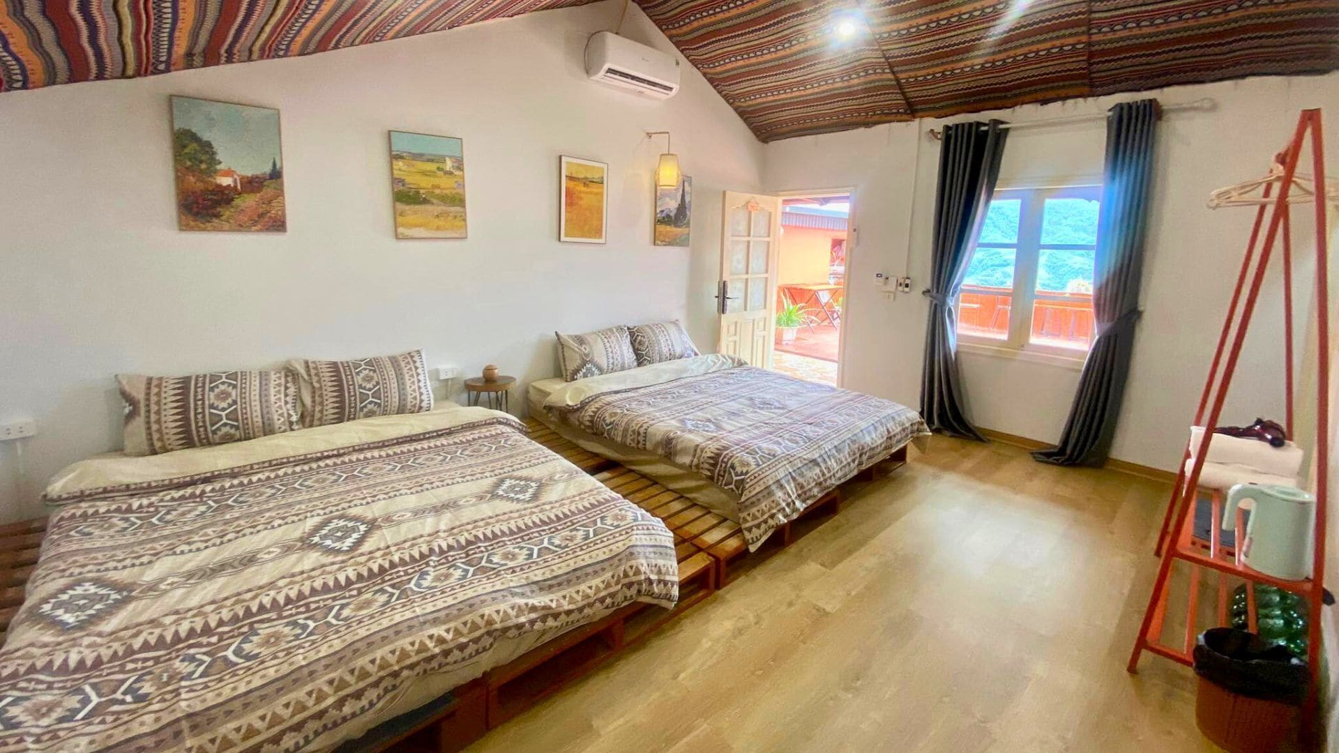 A room with two beds, a wooden ceiling, and a window with curtains.