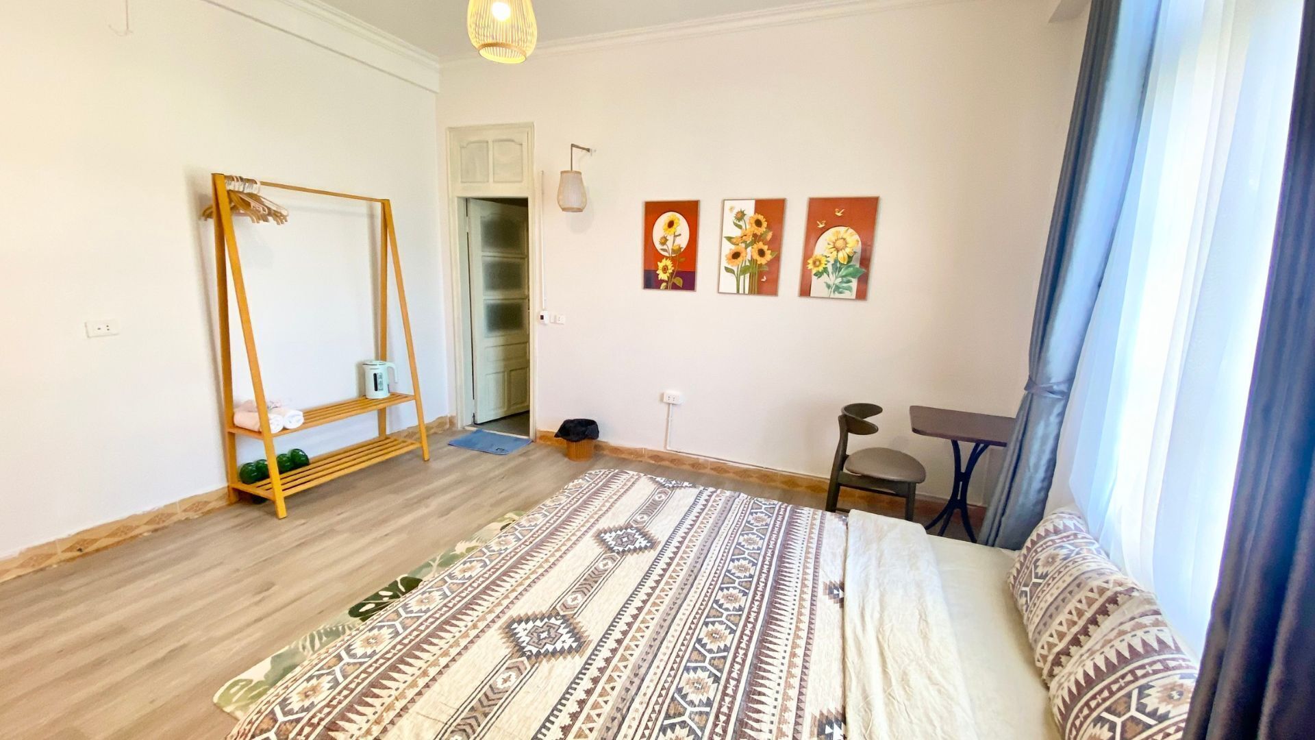 A bedroom with a bed, a wooden ladder, a desk, a chair, and three wall-mounted paintings.