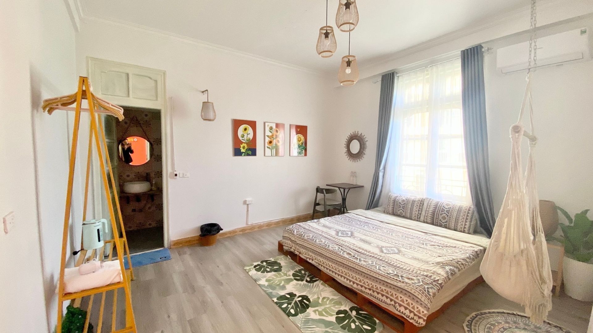 A bedroom with a bed, a hanging chair, a small table, and a window with curtains.