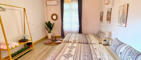 A bedroom with two beds, a hanging chair, a potted plant, and artwork on the walls.