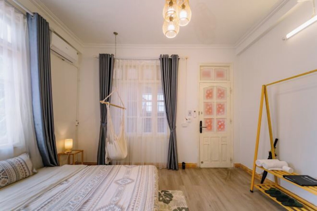 A well-lit bedroom with a bed, a bedside table, a hanging chair, and a wardrobe.