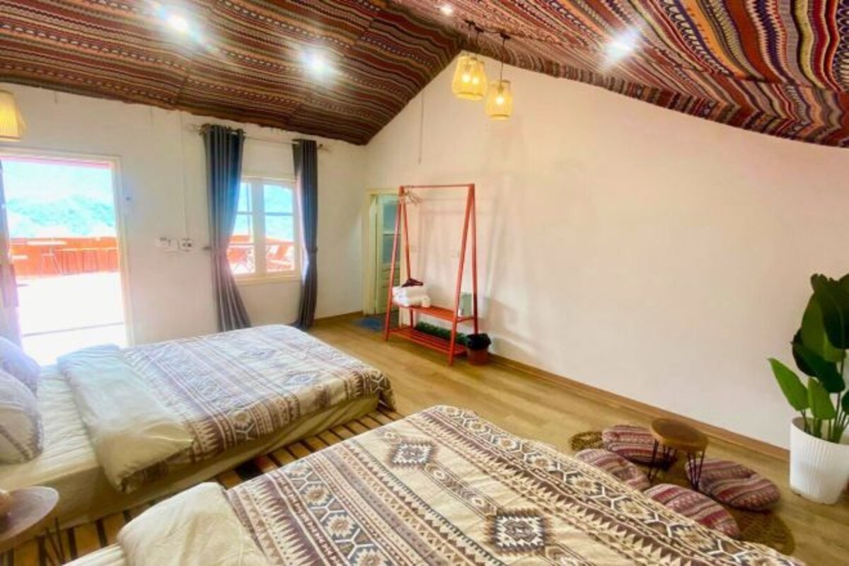 A bedroom with two beds, a canopy bed, a wooden ceiling, and a view of the outdoors.
