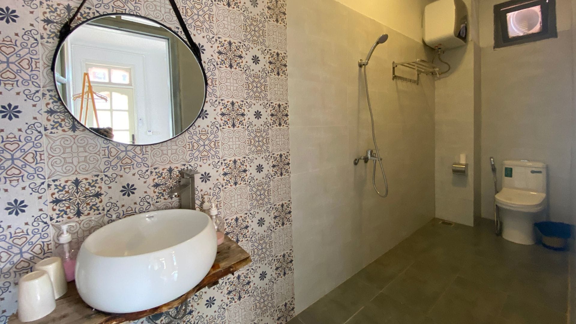 A bathroom with a round mirror, a white sink, a shower, and a toilet.