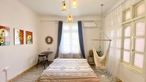 Un dormitorio con una cama grande, un escritorio, una silla, un sillón colgante y una ventana con cortinas.
