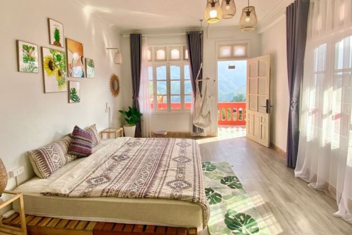 A bedroom with a bed, a window, and a view of a balcony.