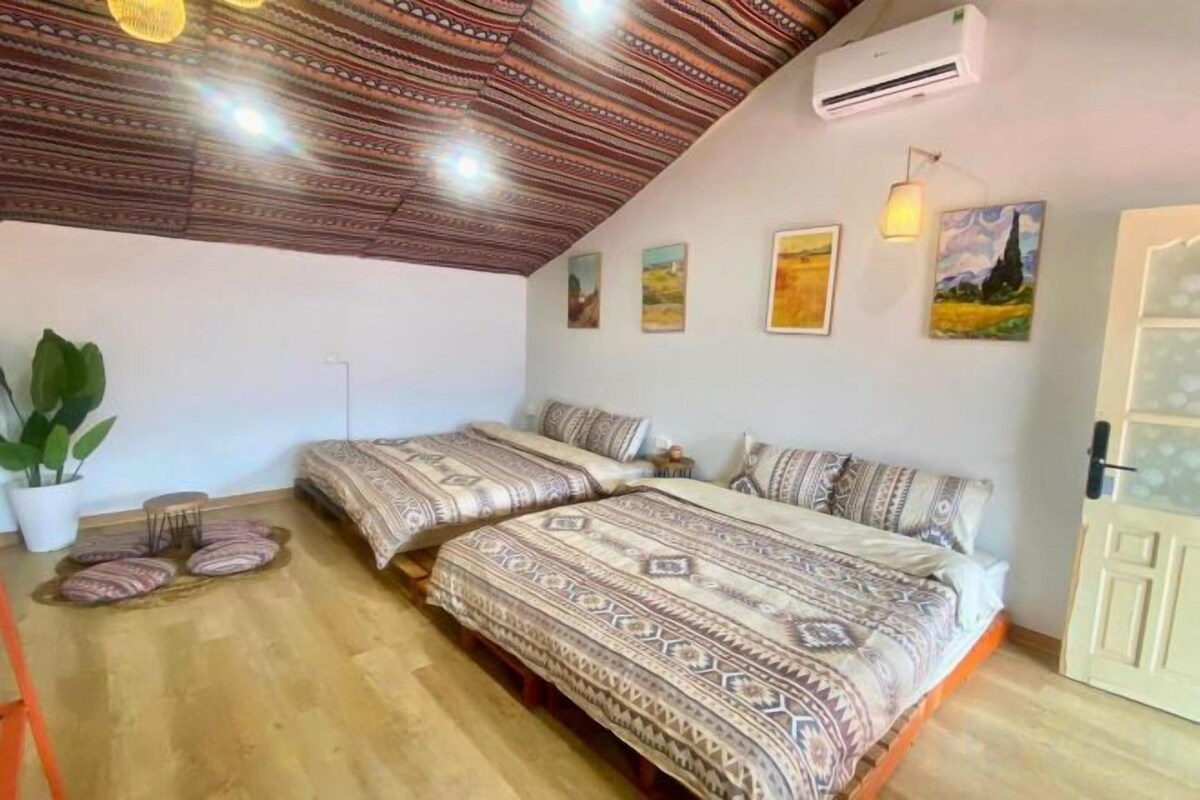 A room with two beds, a potted plant, and a ceiling with a patterned design.