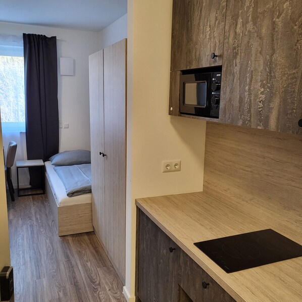 A compact room with a bed, a small desk, and a kitchenette area. - Bader Aparthotel (Unterschleißheim)