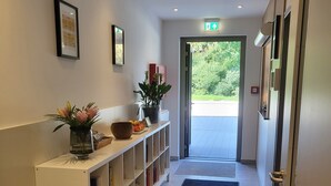 A hallway with a white reception desk, a black carpet, and a door leading outside. - Bader Aparthotel (Unterschleißheim)