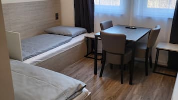 Ein kleines Zimmer mit zwei Einzelbetten, einem Tisch und einem Stuhl.