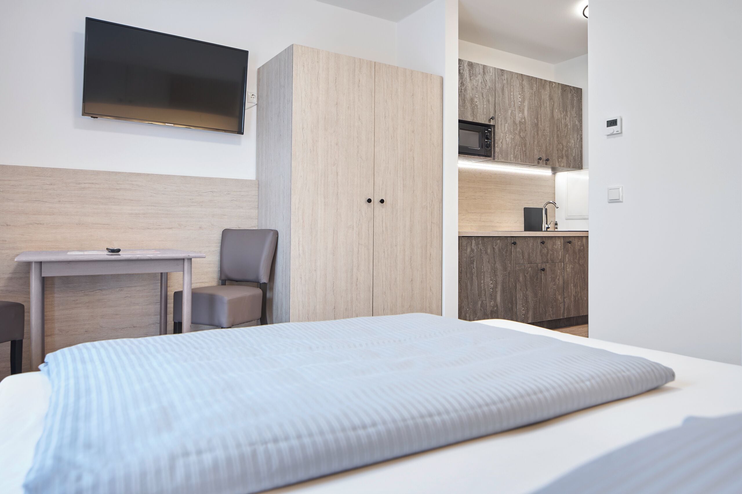 Een moderne hotelkamer met een bed, een bureau, een stoel, een televisie en een kitchenette.
