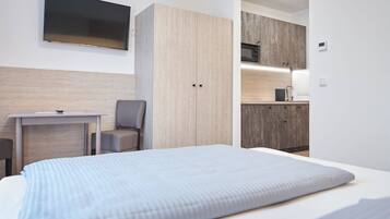 Een moderne hotelkamer met een bed, een bureau, een stoel, een televisie en een kitchenette.