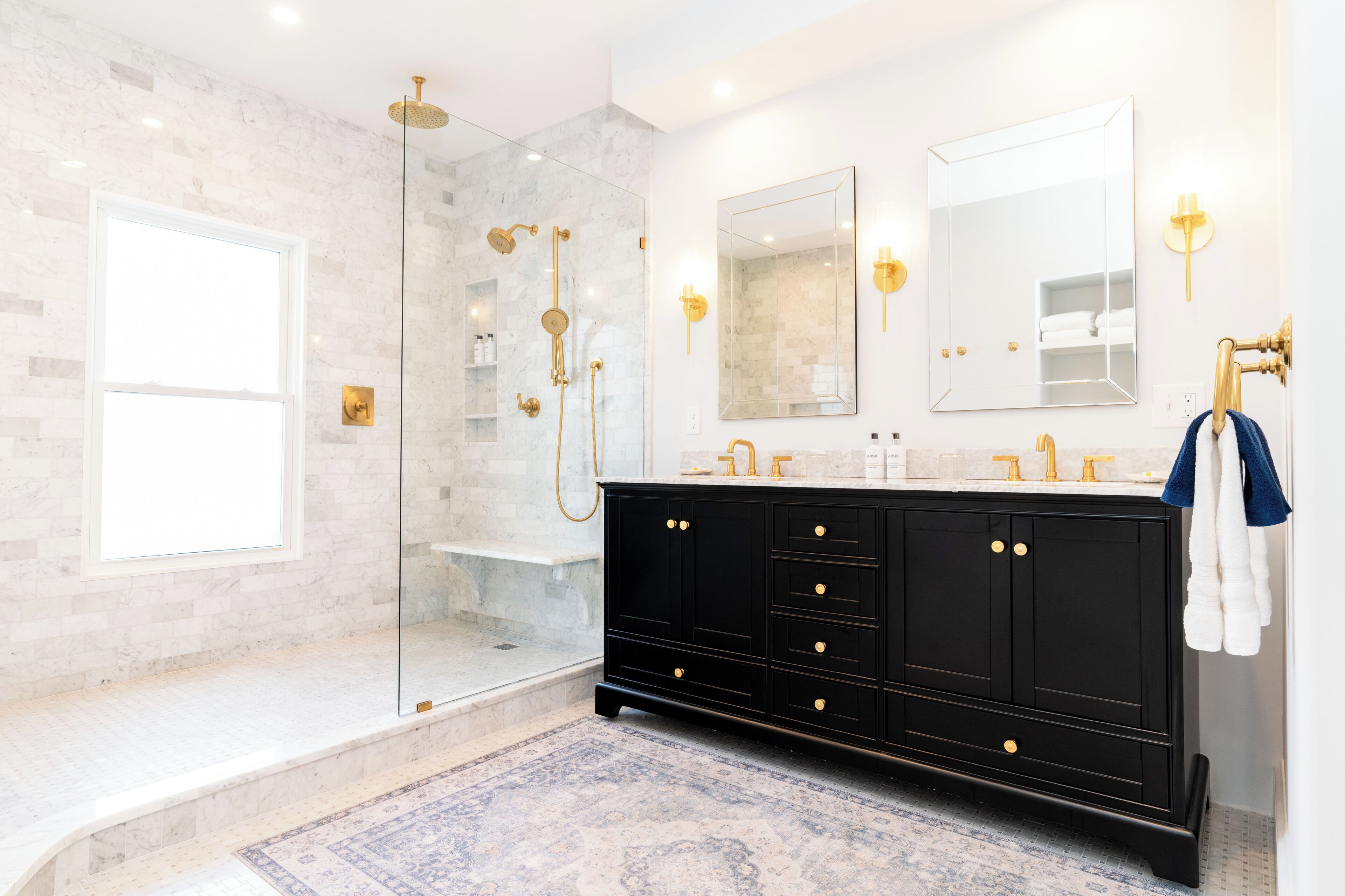 A modern bathroom with a glass-enclosed shower, a black vanity with gold fixtures, and a large mirror.