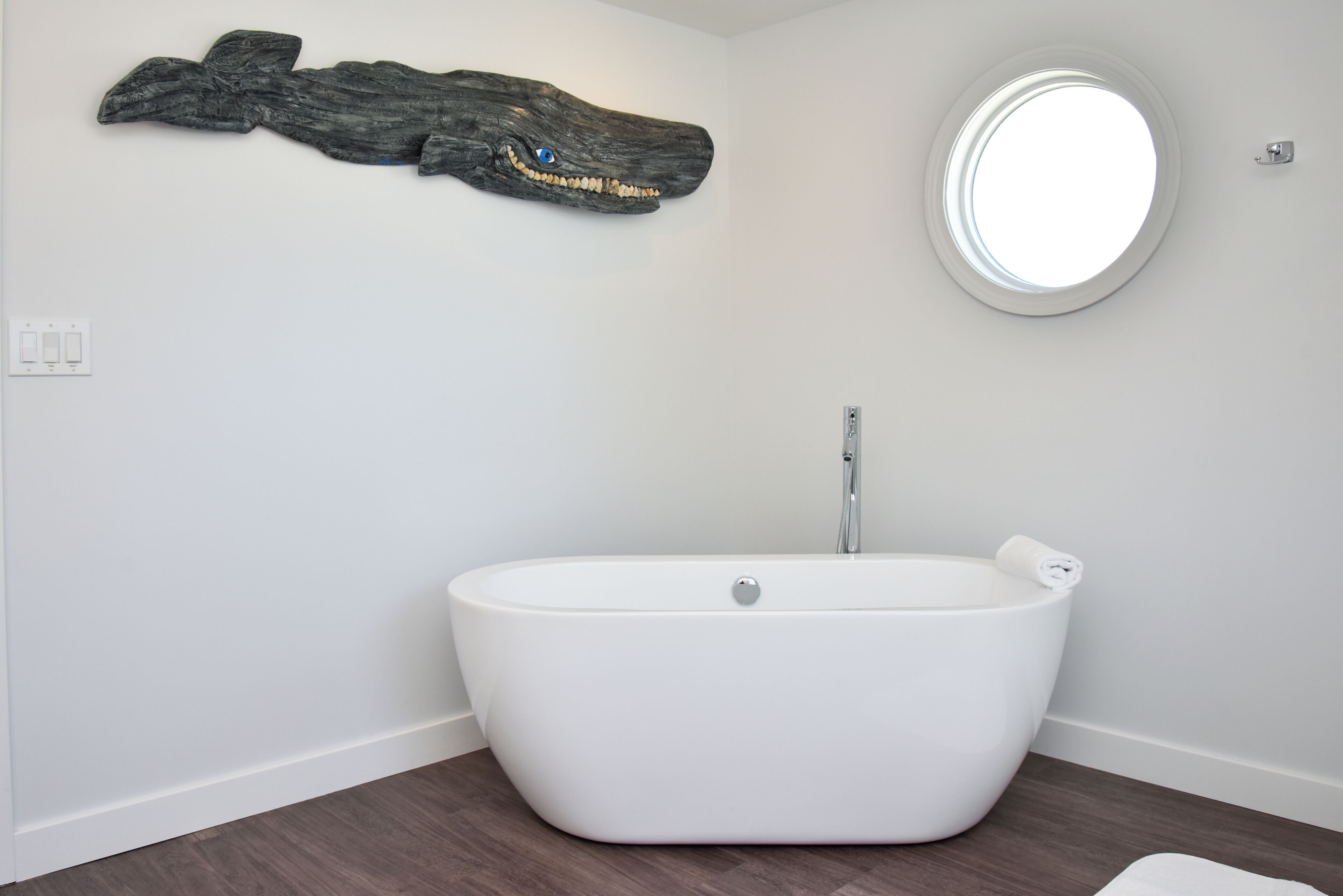 A modern bathroom with a freestanding bathtub, a round mirror, and a wooden wall art piece.