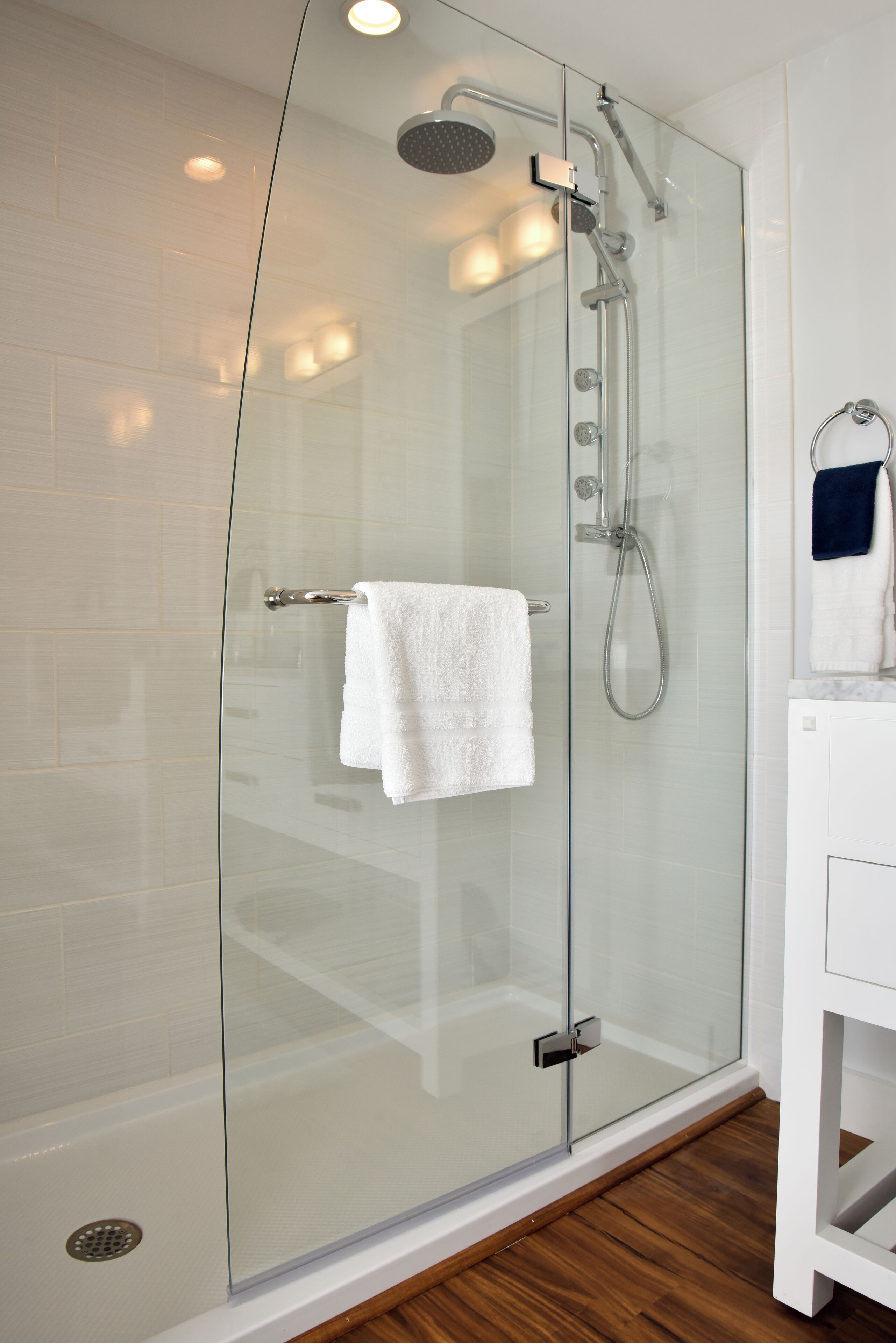A modern bathroom with a glass-enclosed shower, white tiles, and a wooden floor.