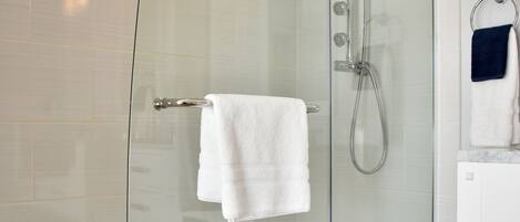 A modern bathroom with a glass-enclosed shower, white tiles, and a wooden floor.