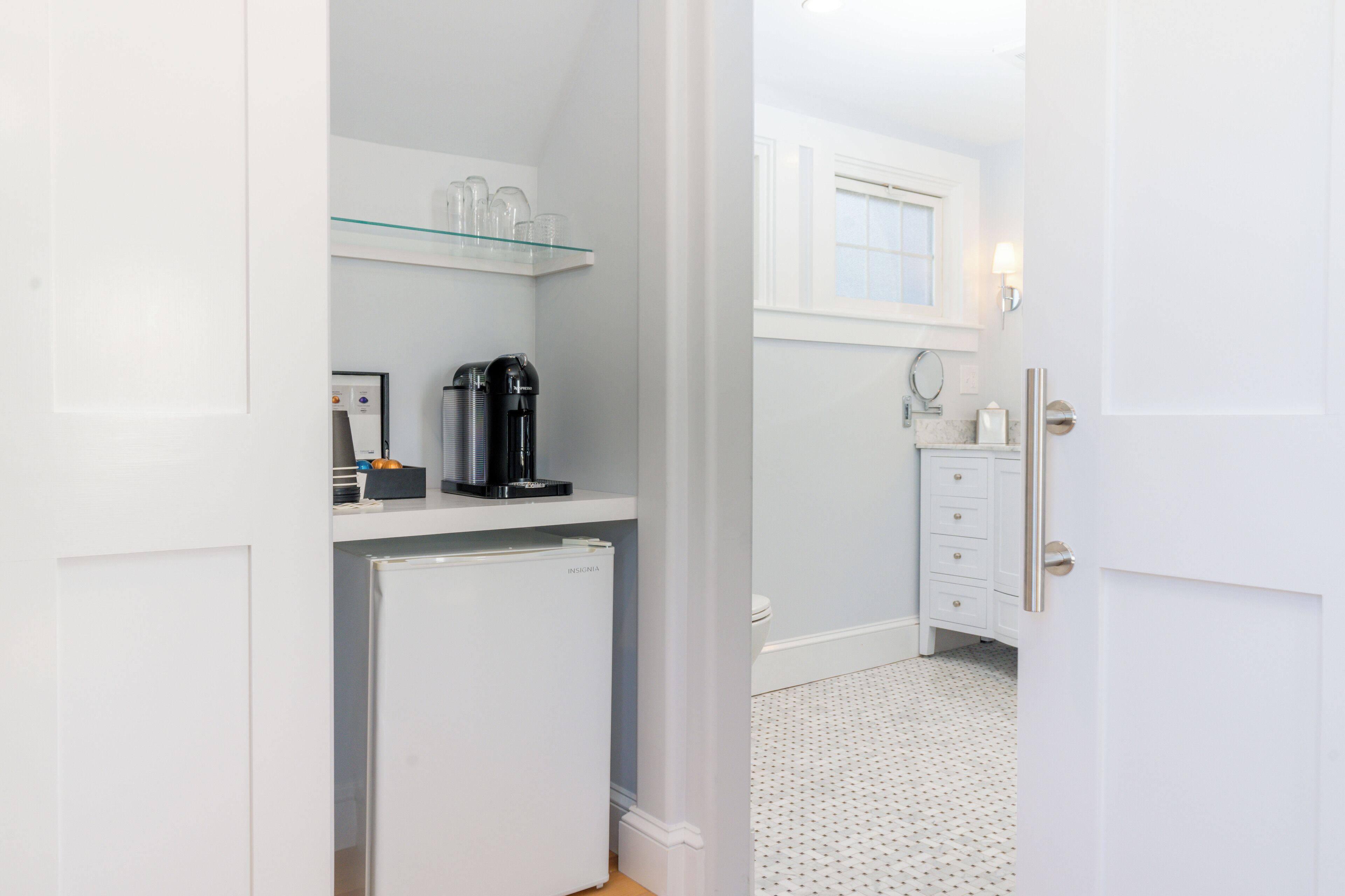 A compact kitchen with a refrigerator, coffee maker, and glass shelves.