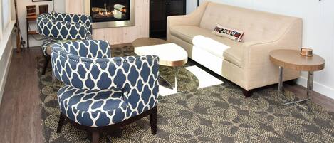A living room with a beige sofa, patterned armchairs, a flat-screen TV, a fireplace, and a small round table.