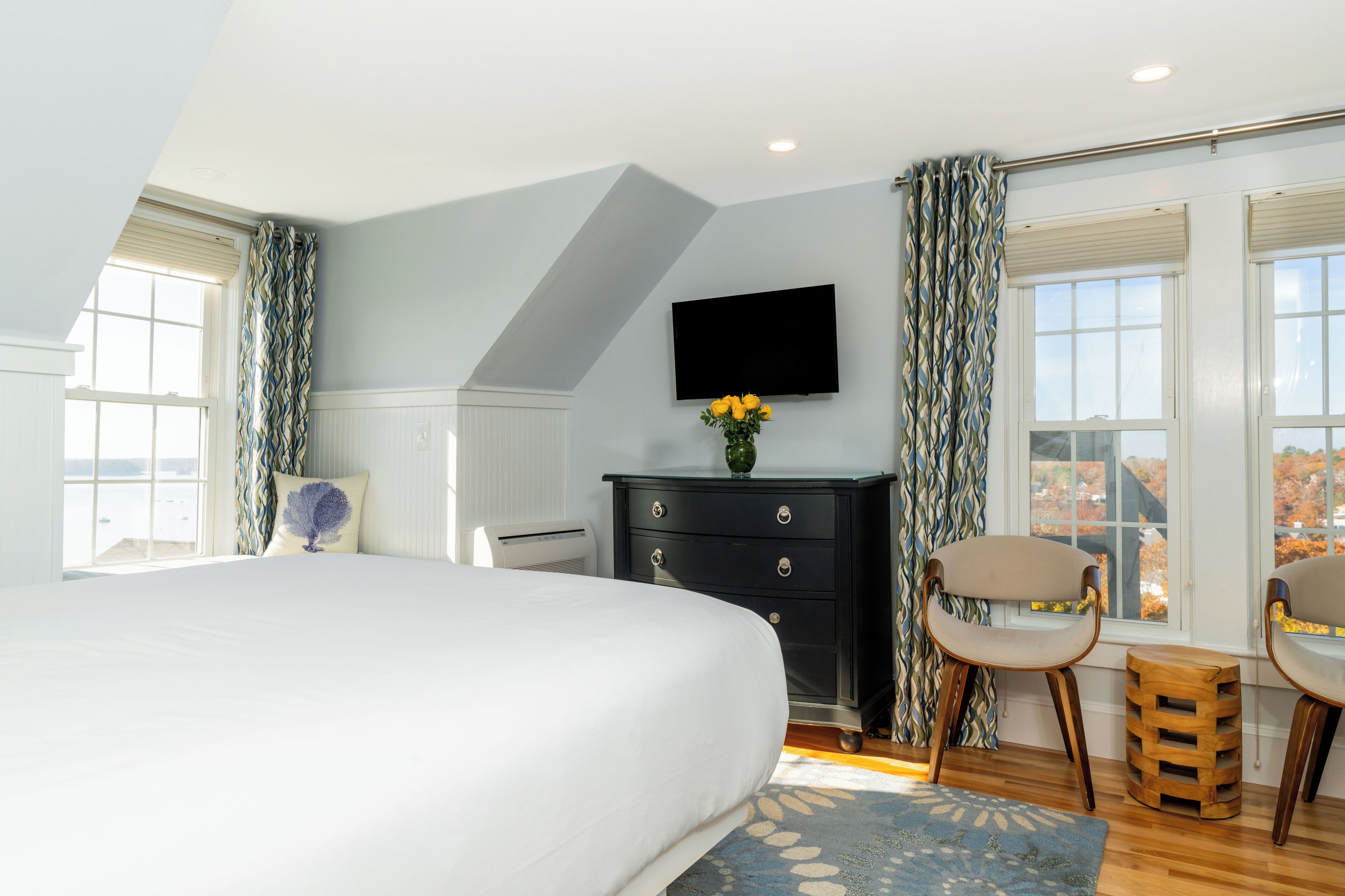A bedroom with a large bed, a dresser, two chairs, a TV, and a window with curtains.