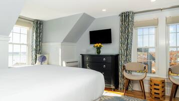 A bedroom with a large bed, a dresser, two chairs, a TV, and a window with curtains.