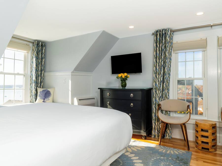 A bedroom with a large bed, a dresser, two chairs, a TV, and a window with curtains.