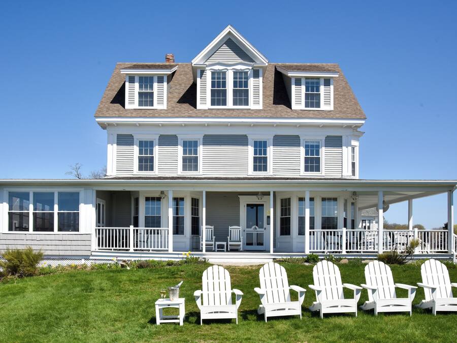Une maison à deux étages avec un porche et quatre chaises Adirondack blanches.
