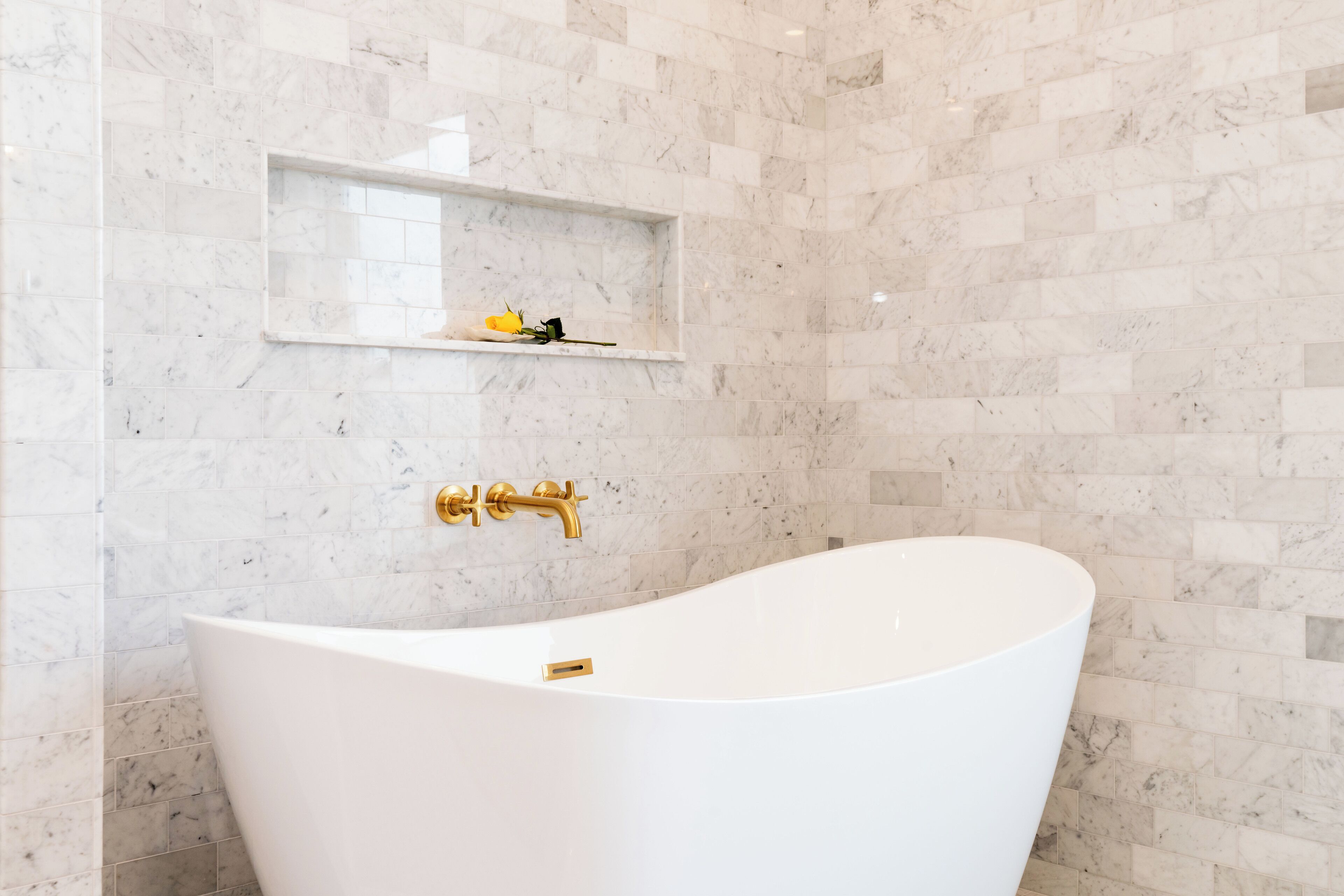 Une salle de bain moderne avec une baignoire sur pieds, des carreaux de marbre et un robinet doré.