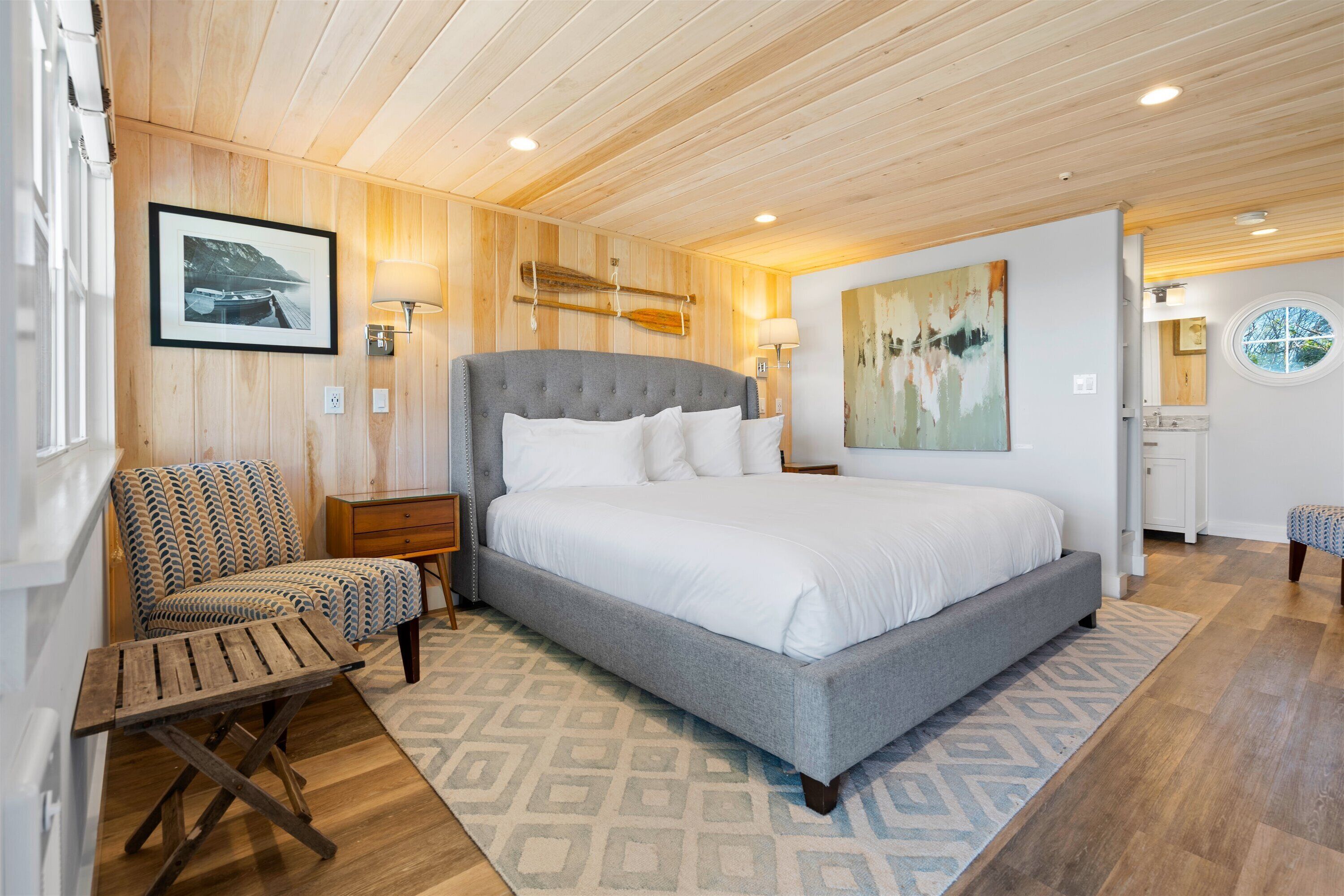 A bedroom with a large bed, a chair, a nightstand, and a wall-mounted lamp.