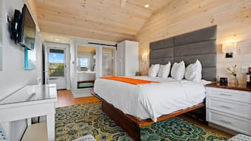 Une chambre avec un plafond en bois, un lit avec une literie blanche et un plaid orange, une table de chevet, une commode et un téléviseur fixé au mur.
