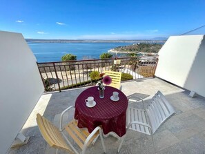 A balcony with a table and chairs, overlooking a body of water and distant land. - Apartment Luky 5 (Dramalj)
