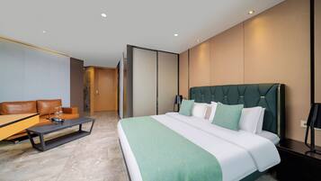 A modern hotel room with a large bed, a sofa, a coffee table, and a desk.