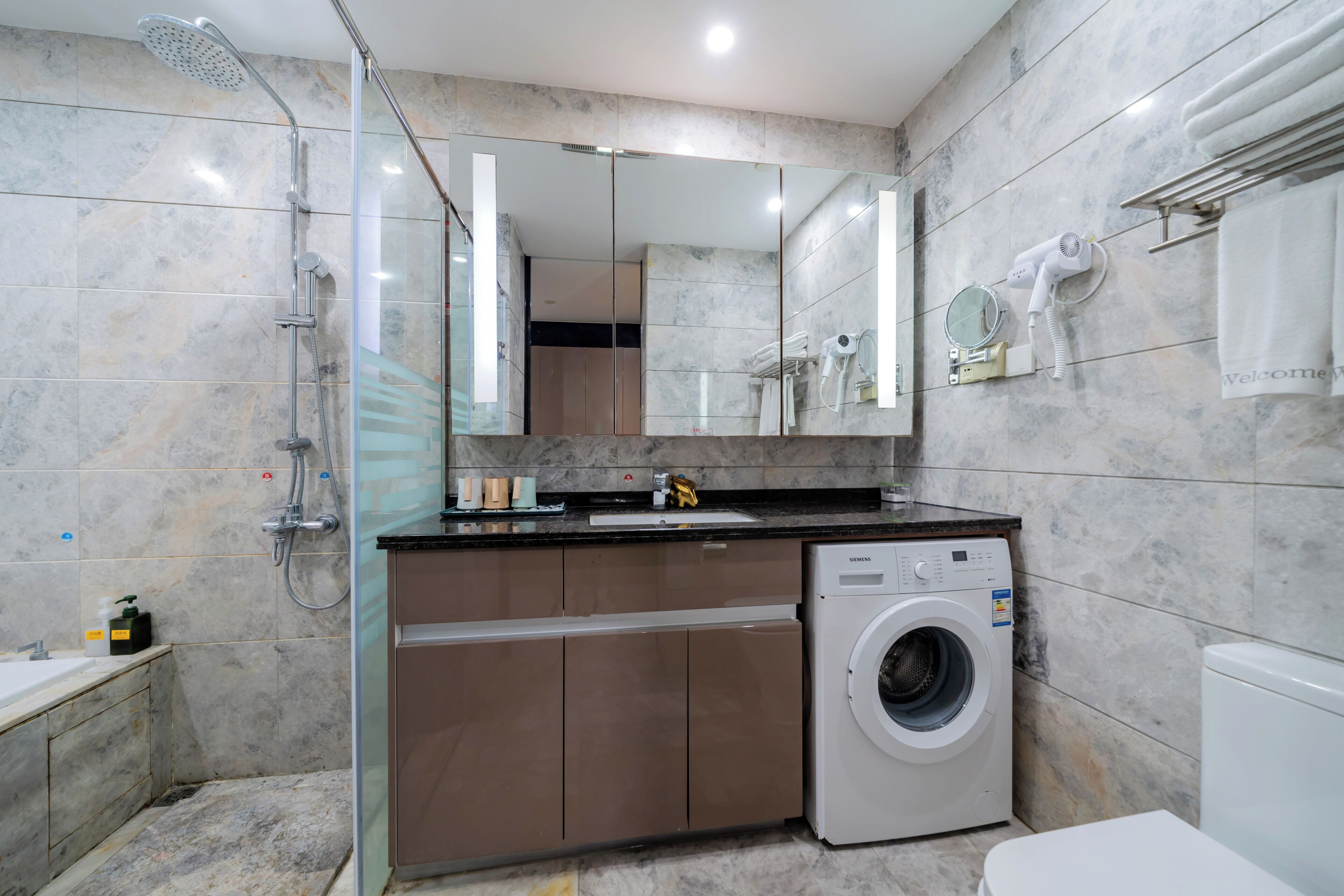 A modern bathroom with a glass-enclosed shower, a built-in washing machine, and a large mirror.