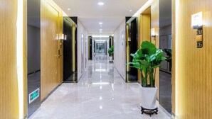 A modern hotel corridor with wooden paneling, a shiny marble floor, and potted plants. - Weekend International Apartment- Beijing Rd A-mall (Guangzhou)
