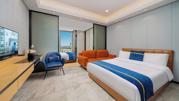A hotel room with a large bed, a desk with a TV, a blue chair, and an orange sofa. - Weekend International Apartment- Beijing Rd A-mall (Guangzhou)