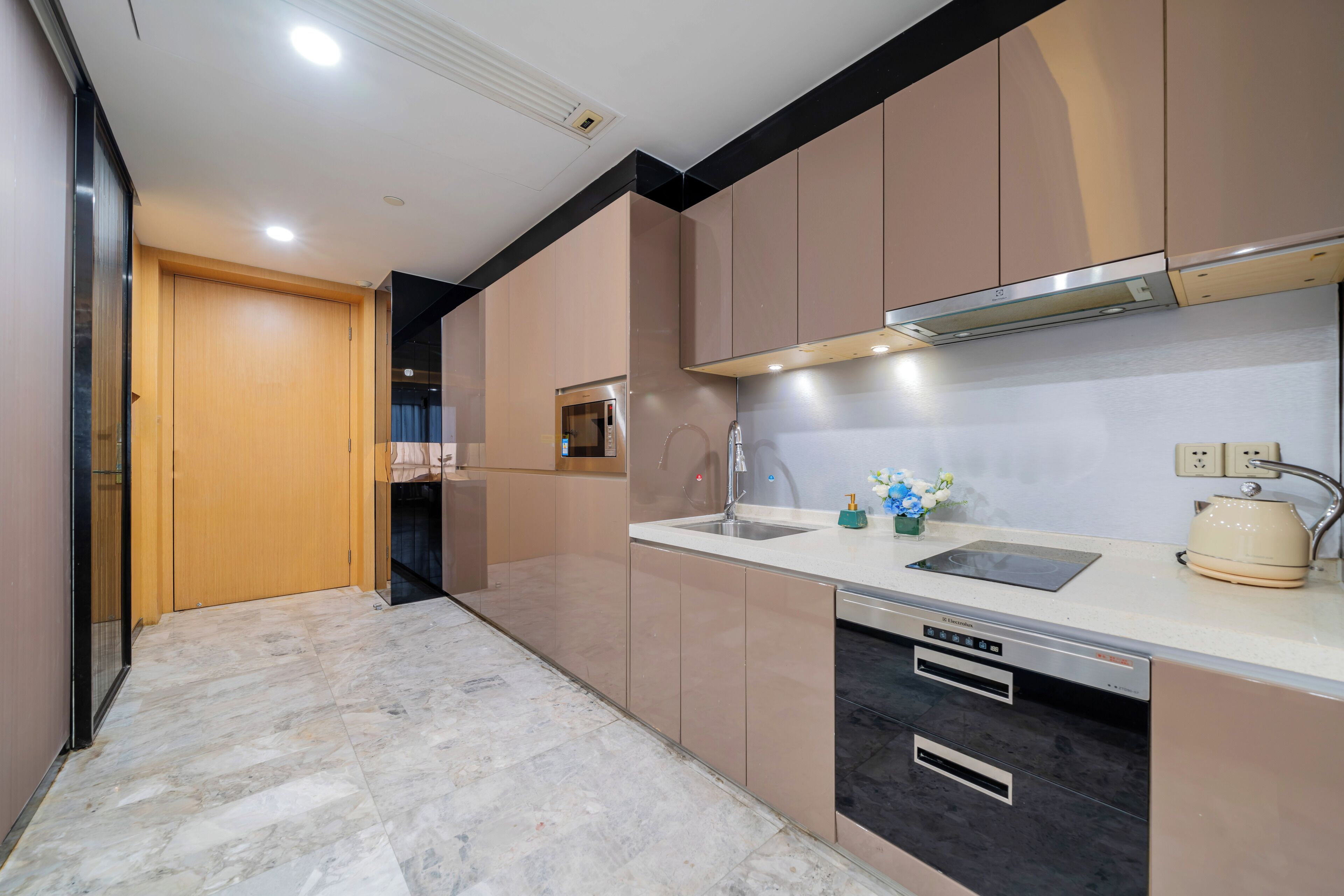 A modern kitchen with a built-in oven, a sink, and a kettle on the countertop.