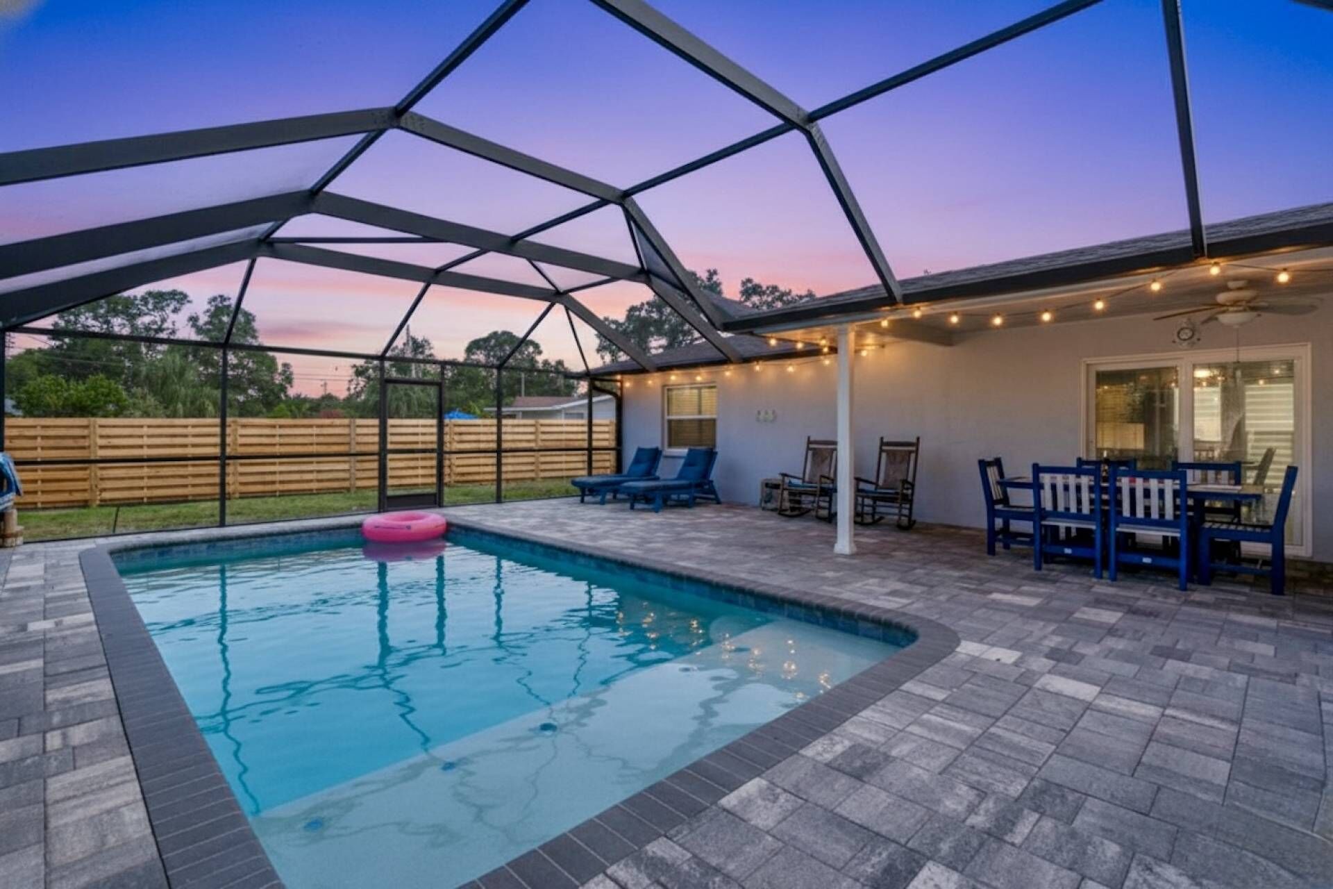 An outdoor swimming pool with a covered patio area, lounge chairs, and string lights.