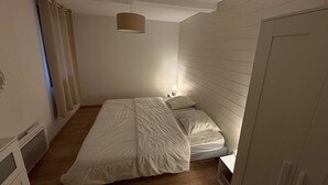 Una habitación pequeña con cama individual, suelo de madera, mesita de noche con lámpara y lámpara en el techo.
